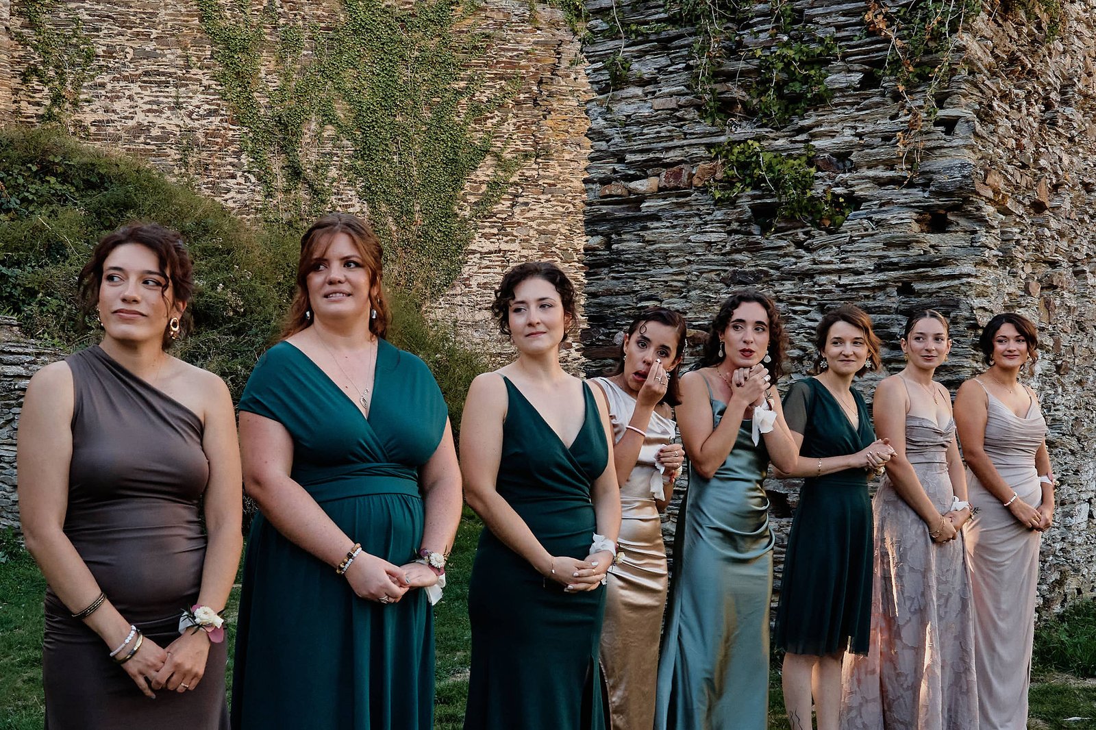 Les témoins alignées devant les remparts regardent arriver la mariée, l’une essuie une larme, une autre a les mains jointes sous le menton