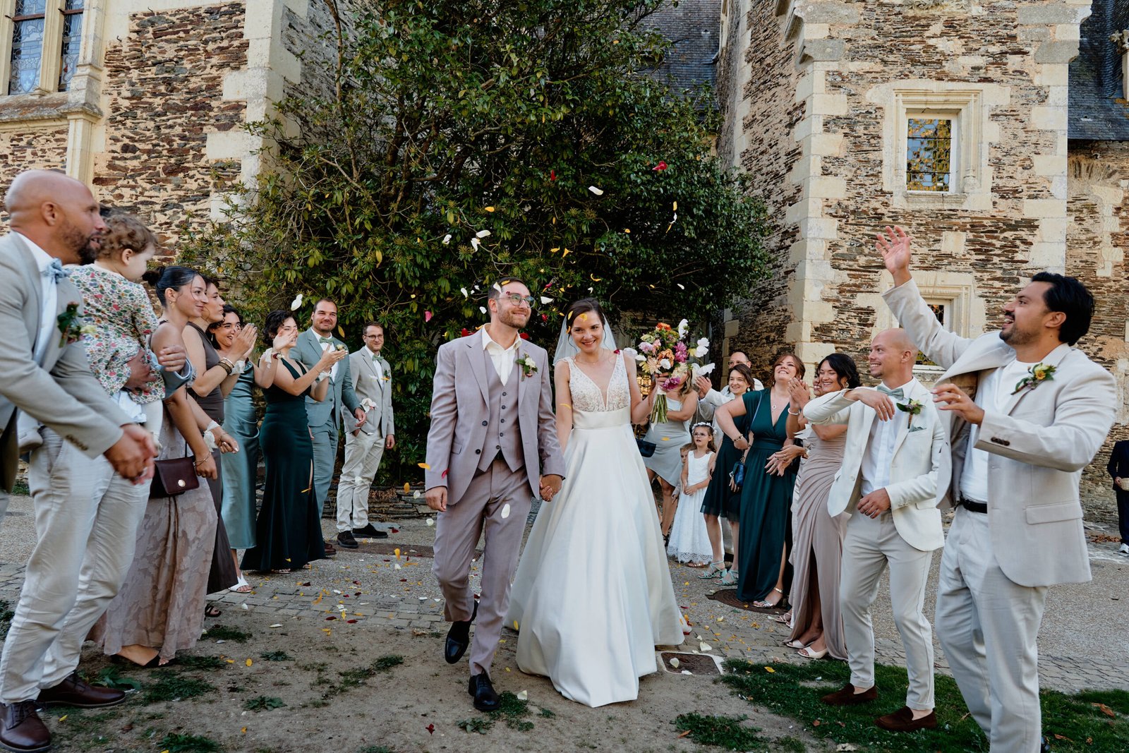 Sortie de cérémonie d’Audrey et Nicolas sous une pluie de pétales, main dans la main, entourés de leurs amis qui applaudissent devant le Château du Plessis-Macé, en Anjou