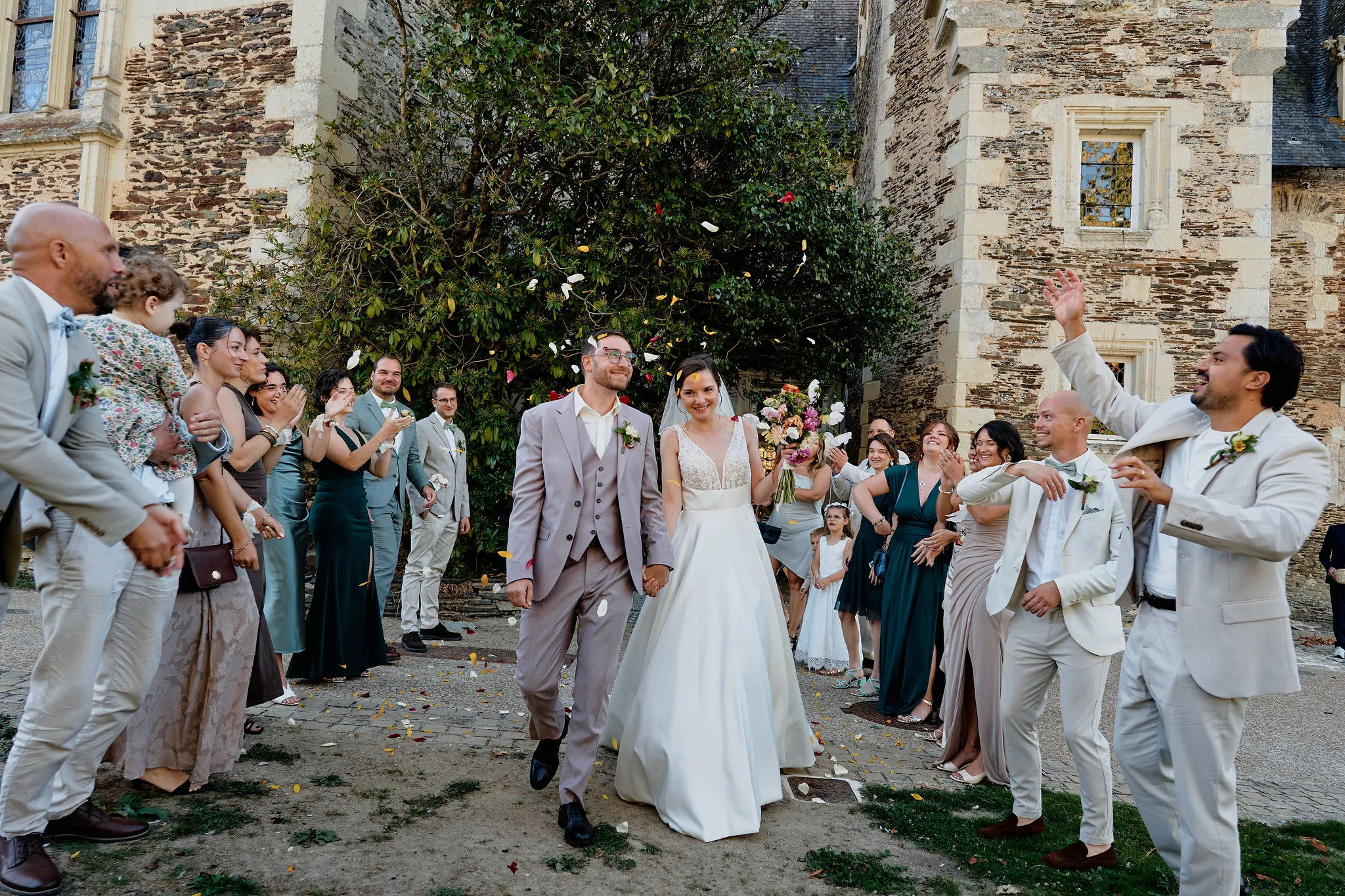Sortie de cérémonie d’Audrey et Nicolas sous une pluie de pétales, main dans la main, entourés de leurs amis qui applaudissent devant le Château du Plessis-Macé, en Anjou
